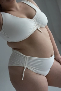 bodya biała góra stroju kąpielowego na modelce – szerokie ramiączka, z marszczeniem, głęboki dekolt, widok z przodu